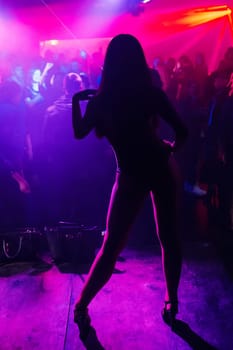 slender young girl dancer with hot body posing nicely on the stage of a nightclub with colored lights silhouette