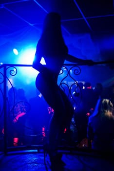 dancer go-go in night club on stage, a dance floor with blue lights and dancing people