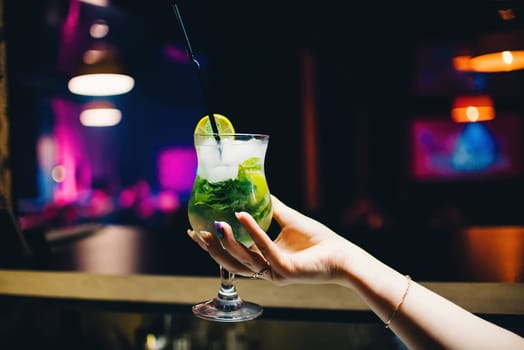 glass of Mojito cocktail in a female hand with a lime and mint with a cooling tube
