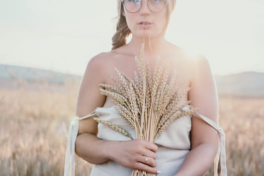 A woman is holding a bunch of wheat in her arms. The wheat is dry and brown, and the woman is wearing a white dress. The scene is set in a field, and the woman is posing for a photo