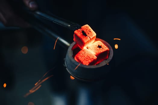 bowl of the hookah with red hot coals in the hands of a hookah on a dark background Smoking area