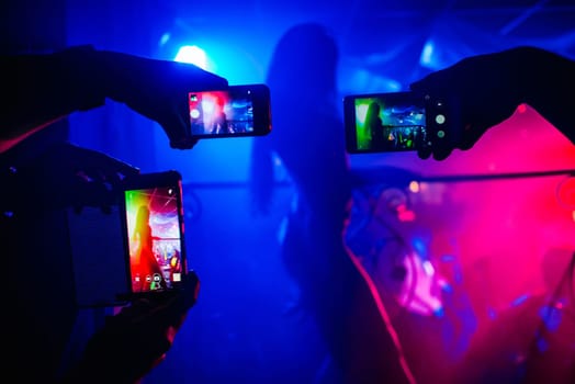 men's hands with smartphones take pictures of a girl dancer in a nightclub