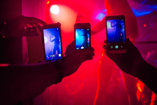 men's hands with smartphones take pictures of a girl dancer in a nightclub