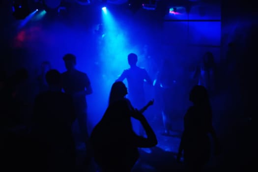 blurred people dancing on the dance floor at the event in a night club under the blue spotlights