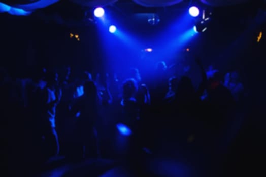 blurred crowd of people on the dance floor in a night club under the blue lights for party and concert