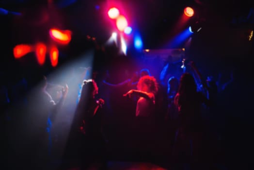 blurred people dancing on the dance floor in a nightclub at a concert party with bright spots of light