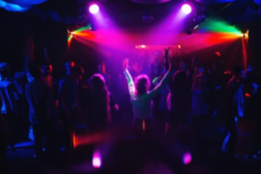 blurred silhouettes of dancing people at a concert with colored lights and spotlights