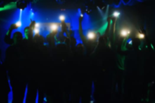 blurred silhouettes of people with lanterns in their hands at the concert in a nightclub