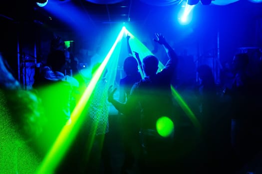 blurred silhouettes of people with their hands up with the laser light in a nightclub