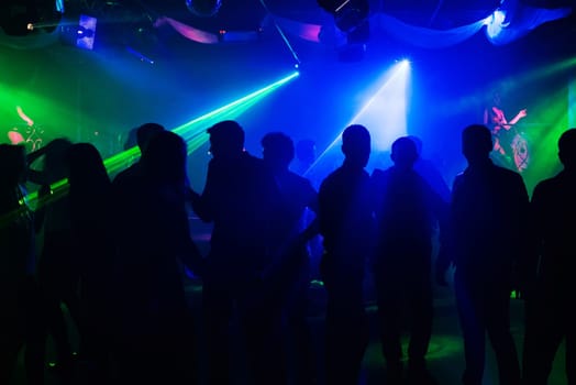 people silhouettes on the dance floor of a night club to laser projectors