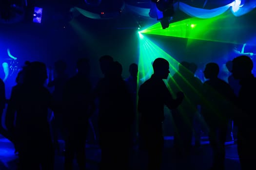 people silhouettes on the dance floor of a night club at the event under the laser lights and concert