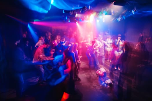 blurred silhouettes of people in a night club at the concert with a moving effect on a long exposure