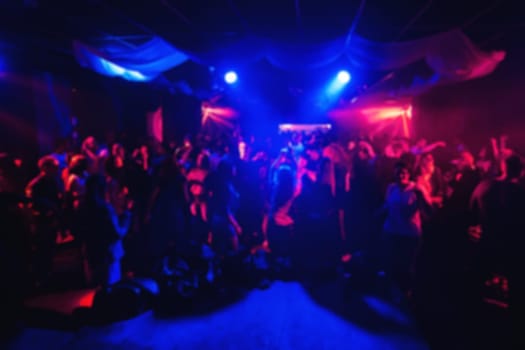 blurred silhouettes of people in the concert hall in a night club under the colourful lighting spotlights