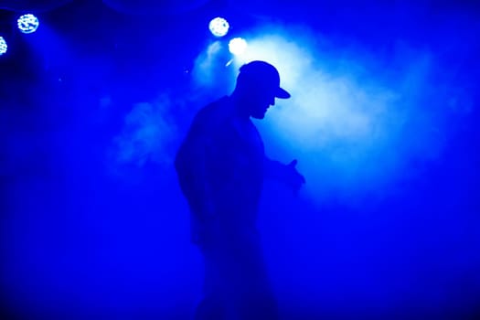 silhouette of the lead in the cap of the rocker on the stage in smoke in a nightclub at a concert