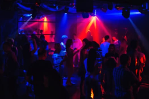 blurred silhouettes of dancing people in night club under the colourful floodlights and spotlights