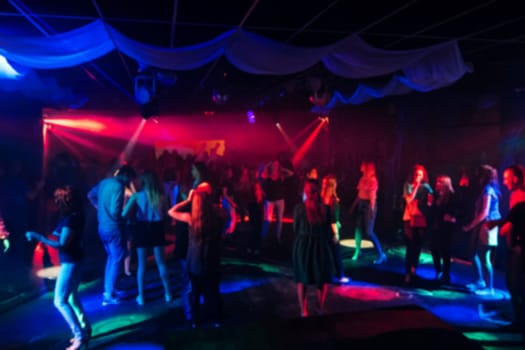 blurred silhouettes of dancing people in night club on the dance floor with brightly coloured lanterns and lights