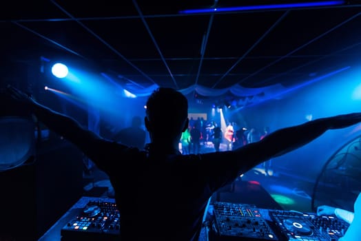 DJ squared his hands on the mixer and remote control the music in the disco nightclub with blue lights