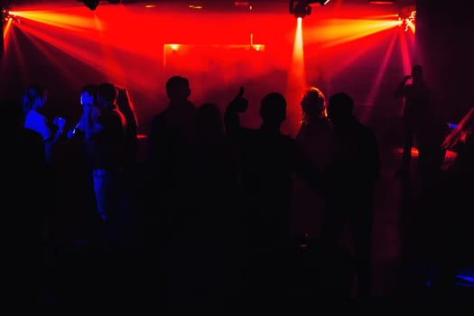 people silhouettes on the dance floor of a night club at the concert under red spotlights