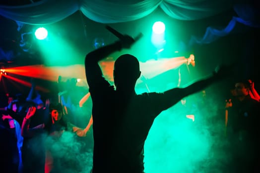 blurred silhouette of the MC with a microphone on stage of nightclub