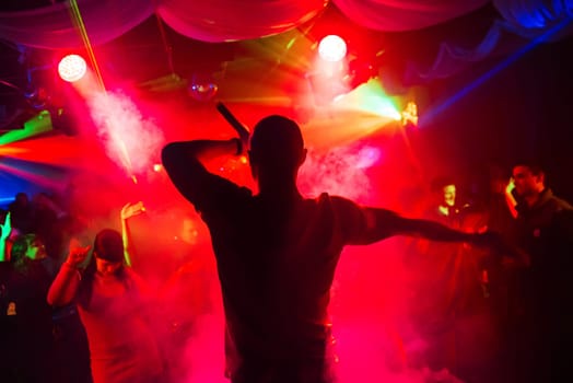blurred silhouette of the MC with a microphone on stage of nightclub
