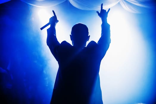 blurred silhouette of the MC with a microphone on stage of nightclub
