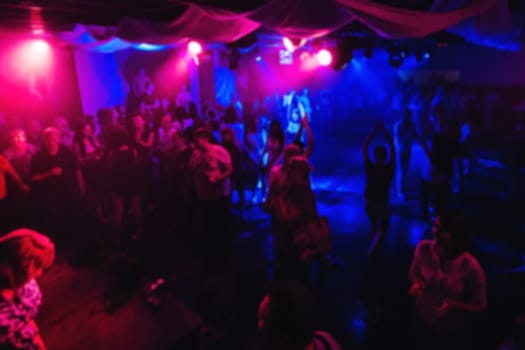 blurred silhouettes of people dancing on the dance floor of a night club at the concert with red and blue abstract background