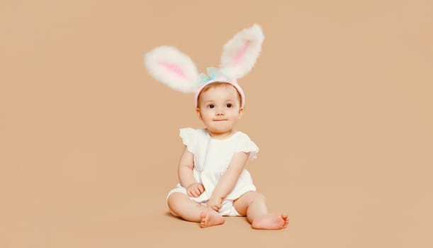 Portrait of cute baby with easter rabbit ears sitting on brown studio background