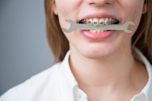 Close-up portrait of a woman with braces holding a wrench in her teeth