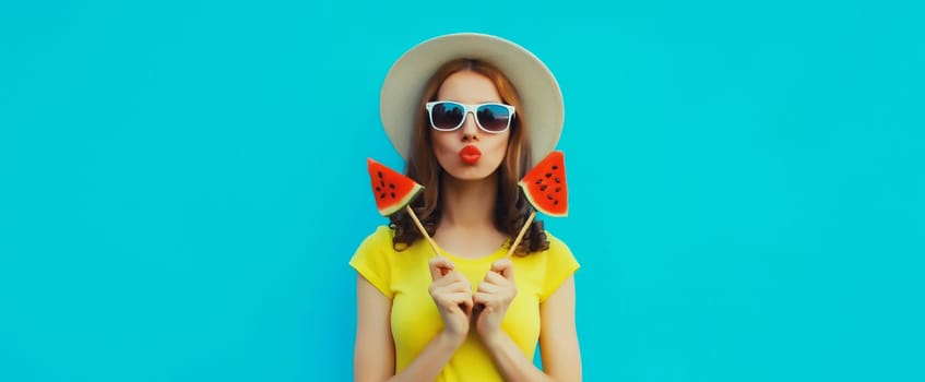 Summer portrait of stylish young woman with sweet juicy lollipop or ice cream shaped slice of watermelon wearing straw hat on blue studio background