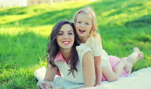 Portrait of happy cheerful smiling mother with little girl child daughter on the grass in sunny summer park