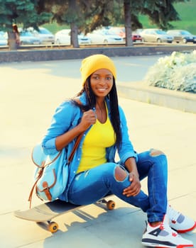 Portrait of stylish happy modern young african woman in colorful bright clothes with skateboard on city street
