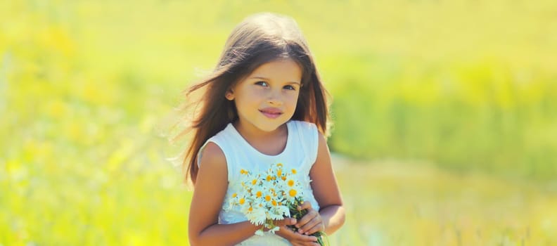 Portrait of cute girl child with wildflowers in sunny summer park