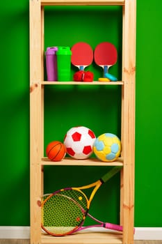 Shelves with different sports equipment against green wall close up