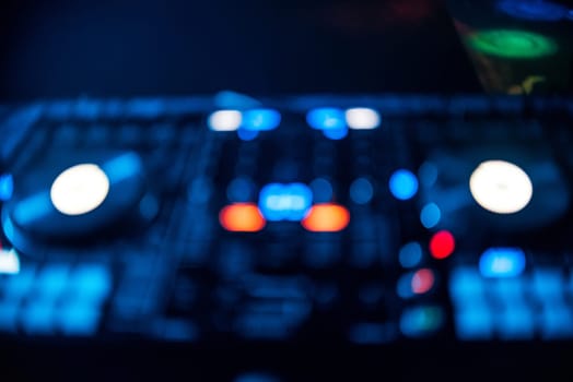 blurred out of focus Board DJ with glowing buttons in a nightclub