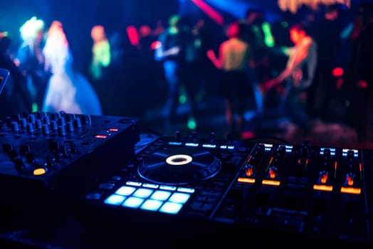 control DJ for mixing music with blurred people dancing at a party in a nightclub