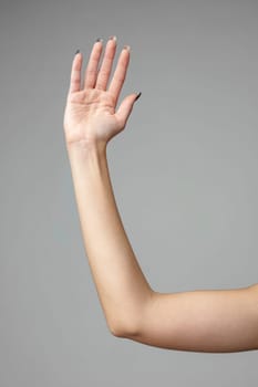 An individuals left hand is raised up against a neutral gray backdrop, displaying an open palm with fingers extended and slightly apart, possibly conveying a sign, signal, or nonverbal communication.