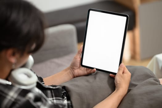 Close up view of young man holding digital tablet with blank desktop screen, lying on a sofa at home.