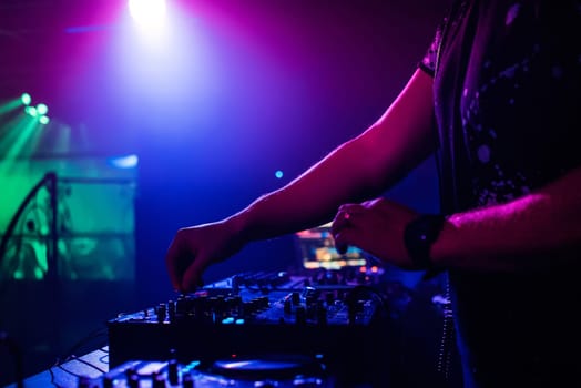 DJ in the night club playing at a professional mixer, color-changing spotlights