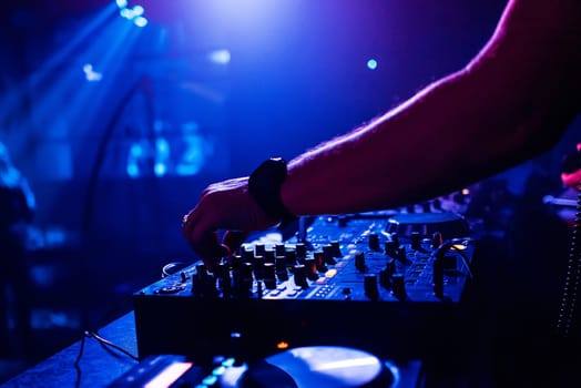 DJ in the night club manages and mixes music on the mixer moving the volume controls