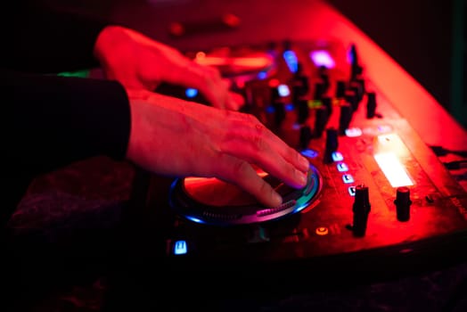 DJ hands mix music on professional mixer in booth at a party in nightclub