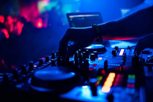 DJ mixing music moving the controllers on the mixer in night club with blue red background