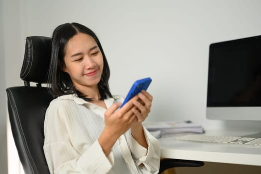 Smiling female office worker using mobile phone at her workplace.