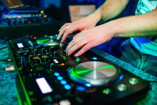 DJ hands mix music on professional mixer in booth at a party in nightclub