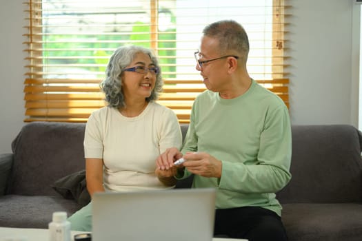 Caring senior husband helping his wife checking blood sugar level at home. Health care concept.