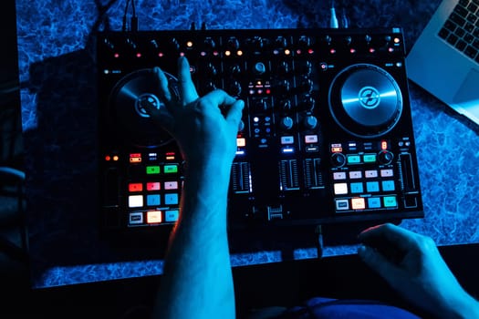 hands of DJ and professional music equipment, mixer buttons and controlling the levels of music and blue lighting