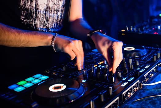 mixer and DJ booth in the nightclub with the hands of a DJ mixing music and control the regulators