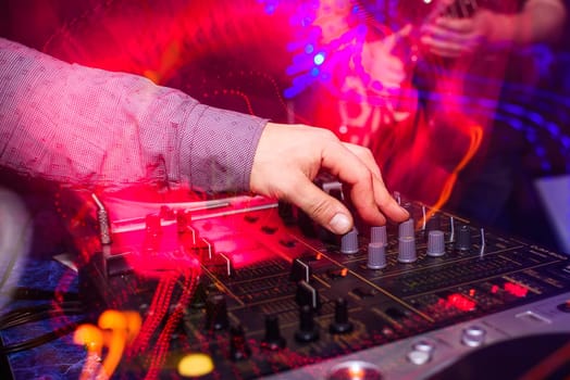 DJ hands mix music on professional mixer in booth at a party in nightclub