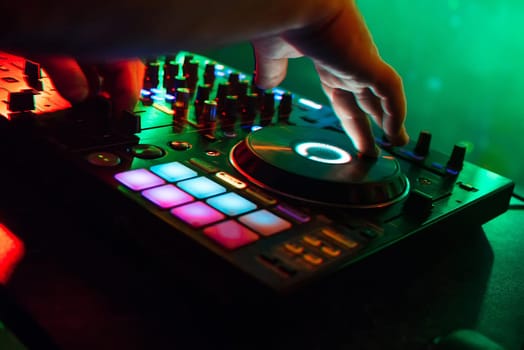 mixer and DJ booth in the nightclub with the arms of the DJ managing the music with colorful lighting and a blurred green background