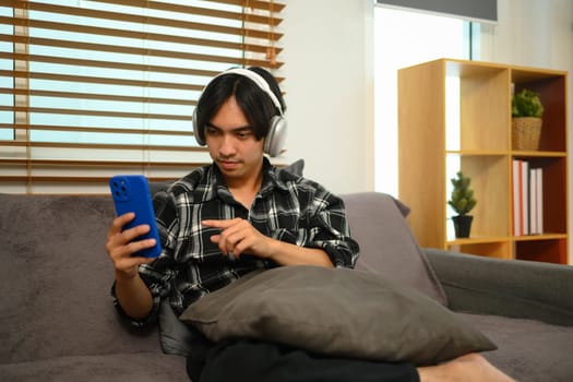 Portrait of man wearing wireless headphones and using smartphone, listening to music online.