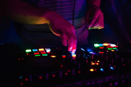 hands on professional DJ mixer with multi-colored glowing buttons mixing music